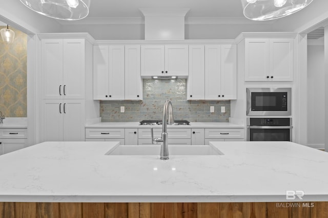 kitchen featuring stainless steel appliances, tasteful backsplash, a kitchen island with sink, white cabinets, and ornamental molding