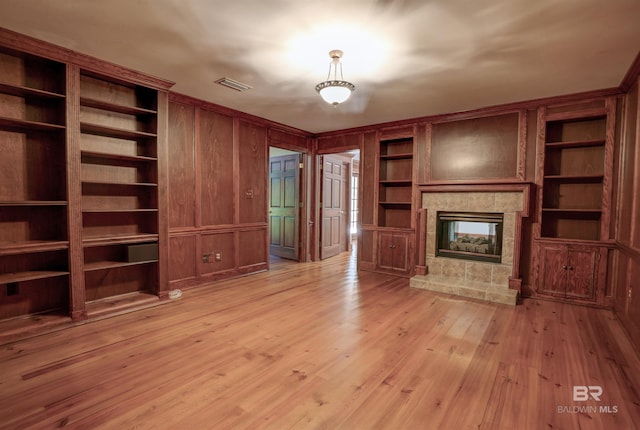 unfurnished living room with a multi sided fireplace, built in features, light hardwood / wood-style flooring, and wood walls