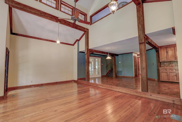 unfurnished living room with light wood-type flooring, high vaulted ceiling, ornamental molding, and french doors