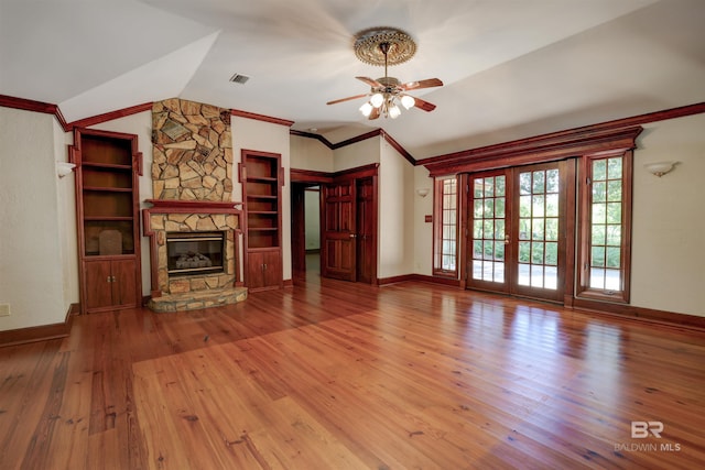 unfurnished living room with vaulted ceiling, a stone fireplace, crown molding, hardwood / wood-style flooring, and ceiling fan