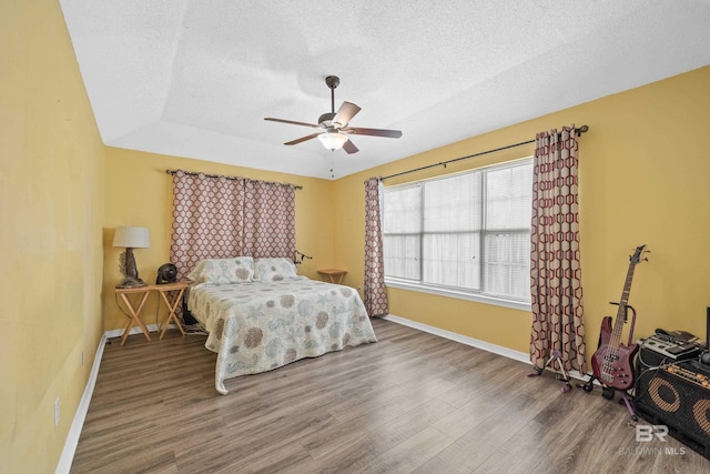 bedroom with ceiling fan, wood finished floors, baseboards, and a textured ceiling