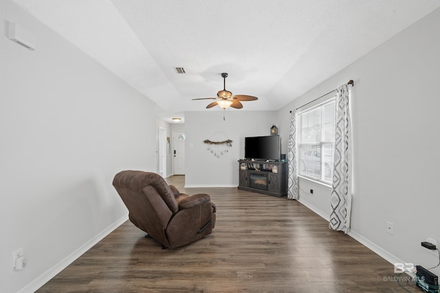 living area with dark wood-type flooring, baseboards, a fireplace, a raised ceiling, and a ceiling fan