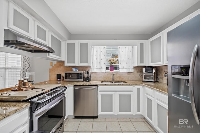 kitchen with under cabinet range hood, appliances with stainless steel finishes, white cabinetry, and a sink