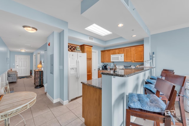 453 Dune Dr Unit 305, Gulf Shores, AL 36542 - kitchen with white appliances, dark stone countertops, light tile patterned floors, a peninsula, and a kitchen bar