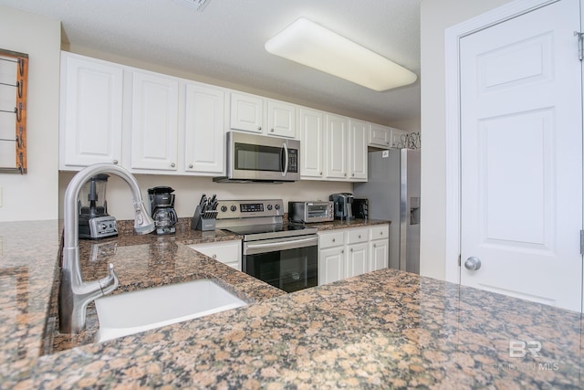 kitchen featuring stainless steel appliances, sink, dark stone countertops, and white cabinets