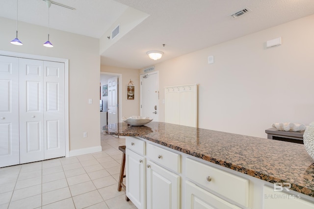 kitchen with light tile patterned flooring, a kitchen breakfast bar, pendant lighting, dark stone counters, and white cabinets