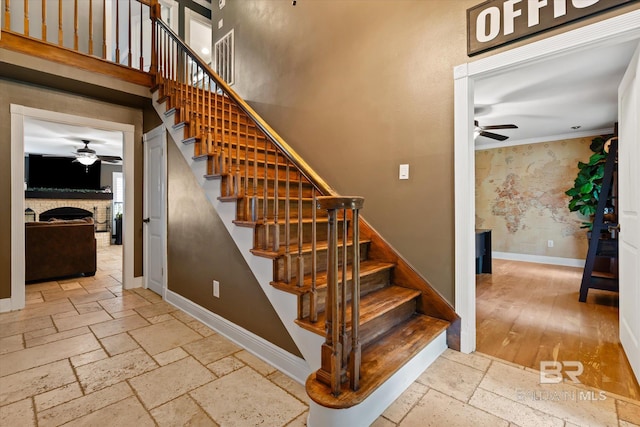 staircase with ceiling fan, hardwood / wood-style flooring, a fireplace, and ornamental molding