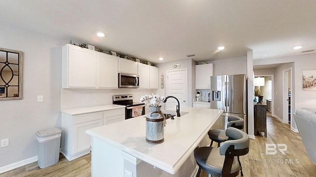 kitchen with stainless steel appliances, a breakfast bar, white cabinetry, light wood-type flooring, and a center island with sink