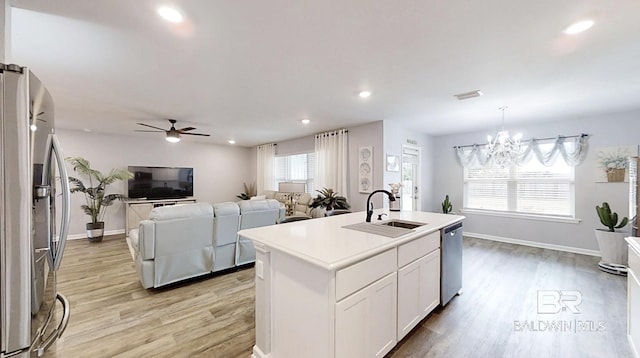 kitchen with open floor plan, stainless steel appliances, light wood-type flooring, white cabinetry, and a sink