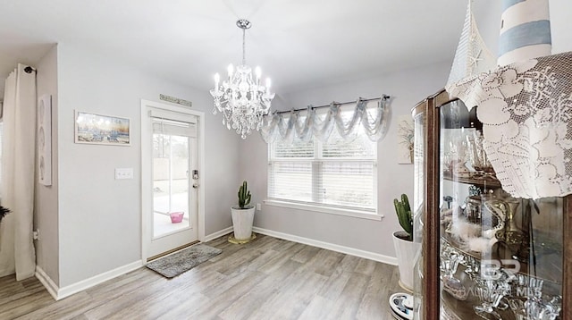 foyer entrance featuring baseboards, light wood finished floors, and a notable chandelier