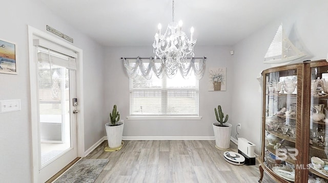 unfurnished dining area with a notable chandelier, baseboards, and wood finished floors