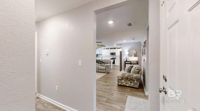 hallway with light wood-style flooring, visible vents, baseboards, and a textured wall