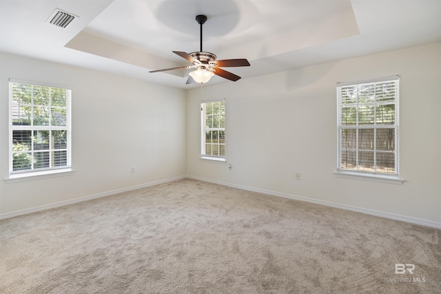 carpeted spare room with ceiling fan, a tray ceiling, visible vents, and baseboards