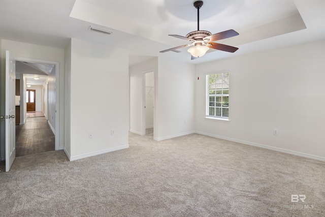 spare room with baseboards, visible vents, a ceiling fan, a tray ceiling, and carpet flooring