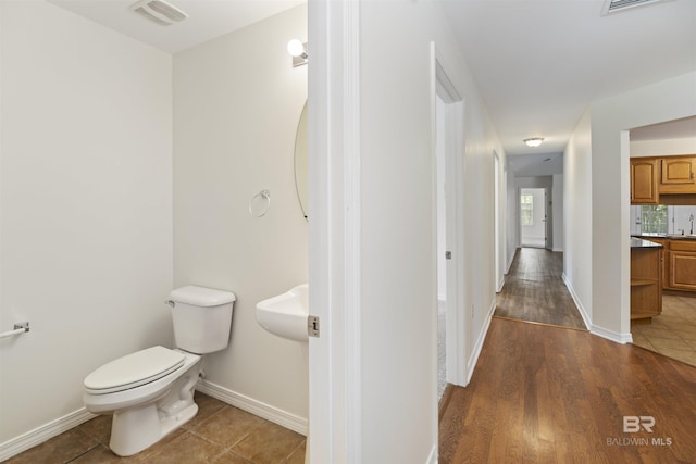 half bath featuring baseboards, visible vents, toilet, tile patterned floors, and a sink