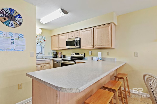 kitchen featuring kitchen peninsula, light tile patterned floors, a breakfast bar, appliances with stainless steel finishes, and light brown cabinets