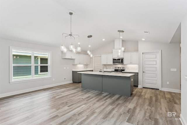 5885 Grotto Ave, Pensacola, FL 32507 - kitchen with stainless steel appliances, a sink, white cabinetry, light wood-style flooring, and a center island with sink
