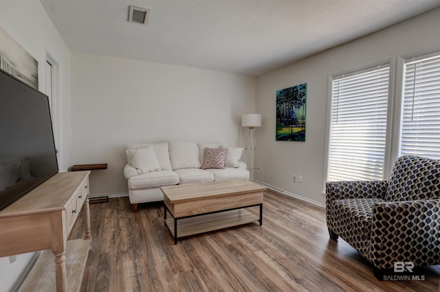 living area featuring visible vents, a textured ceiling, baseboards, and wood finished floors