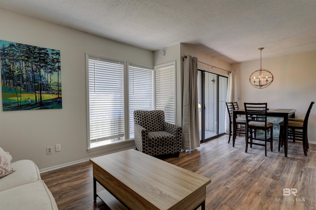 living room with dark wood-style floors, a notable chandelier, a textured ceiling, and baseboards