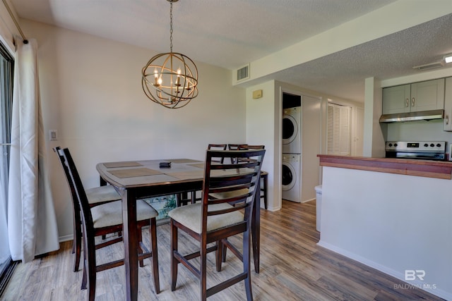 dining area with stacked washer and dryer, visible vents, a textured ceiling, a chandelier, and light wood-type flooring