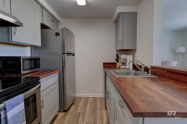 kitchen featuring appliances with stainless steel finishes, butcher block counters, a sink, and exhaust hood