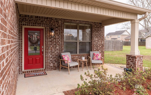 view of exterior entry featuring brick siding, a lawn, and fence