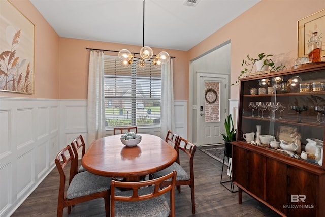 dining area with an inviting chandelier, dark wood-style floors, and wainscoting