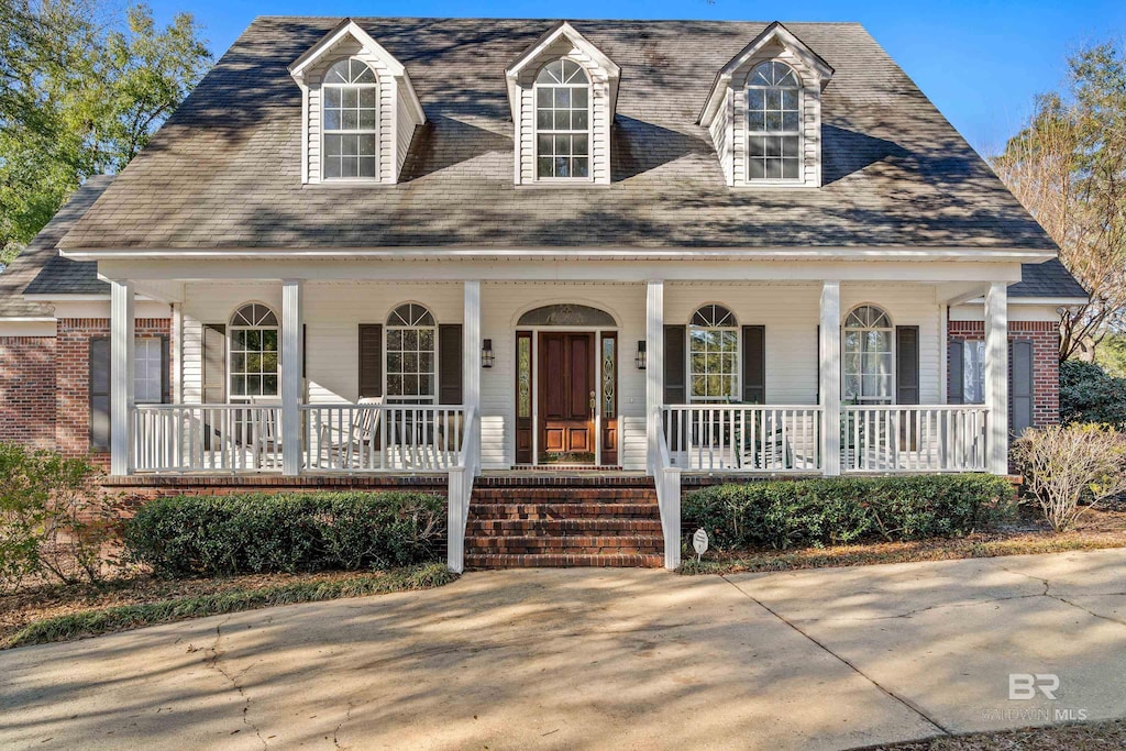 cape cod house with brick siding and a porch