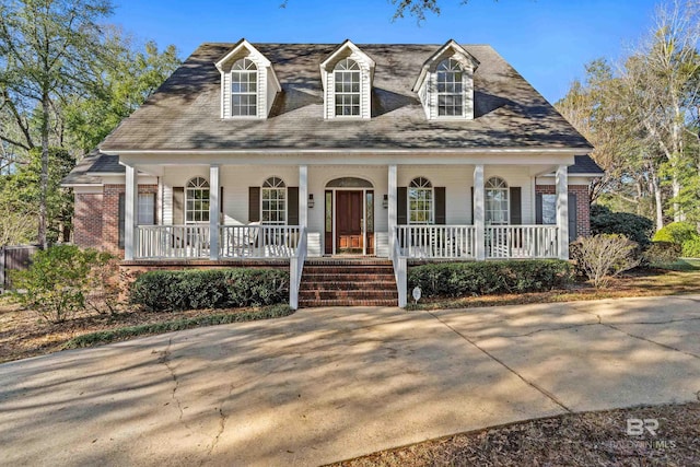 cape cod home featuring brick siding and a porch