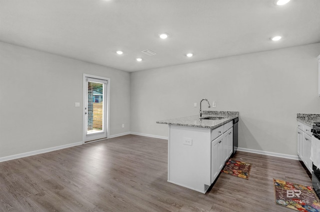 kitchen featuring kitchen peninsula, light stone countertops, sink, wood-type flooring, and white cabinets