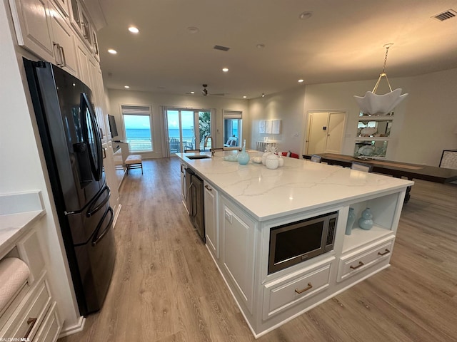 kitchen featuring light stone countertops, a center island with sink, light hardwood / wood-style flooring, white cabinetry, and stainless steel microwave