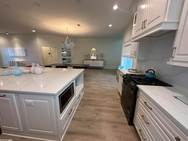 kitchen with light stone countertops, white cabinetry, stainless steel microwave, light hardwood / wood-style floors, and black range with gas stovetop