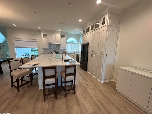 kitchen with white cabinetry, sink, an island with sink, light wood-type flooring, and a breakfast bar area