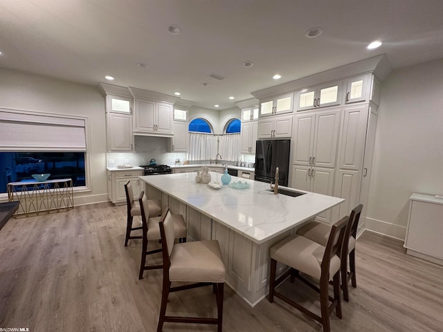 kitchen with light hardwood / wood-style flooring, a kitchen bar, white cabinetry, and black appliances