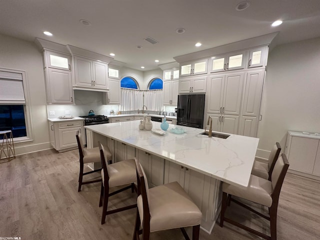 kitchen featuring black refrigerator with ice dispenser, a kitchen bar, light hardwood / wood-style floors, and white cabinets