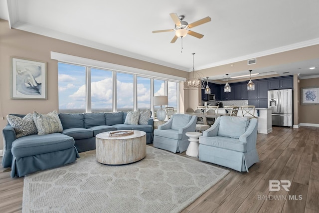 living room featuring ceiling fan with notable chandelier, hardwood / wood-style floors, and crown molding