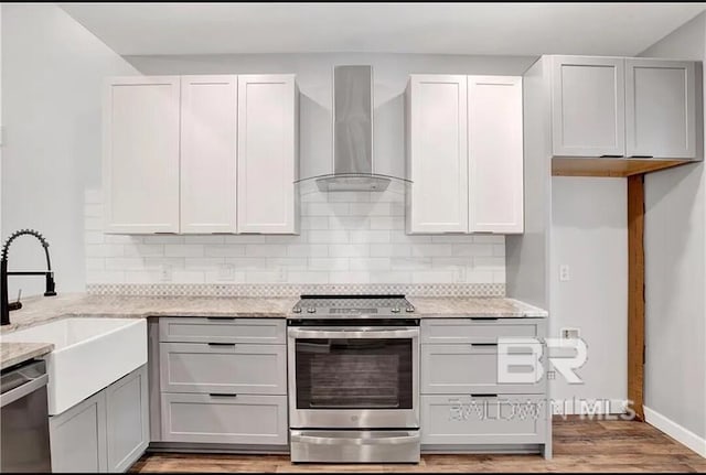 kitchen featuring sink, stainless steel appliances, light stone countertops, wall chimney range hood, and light hardwood / wood-style flooring