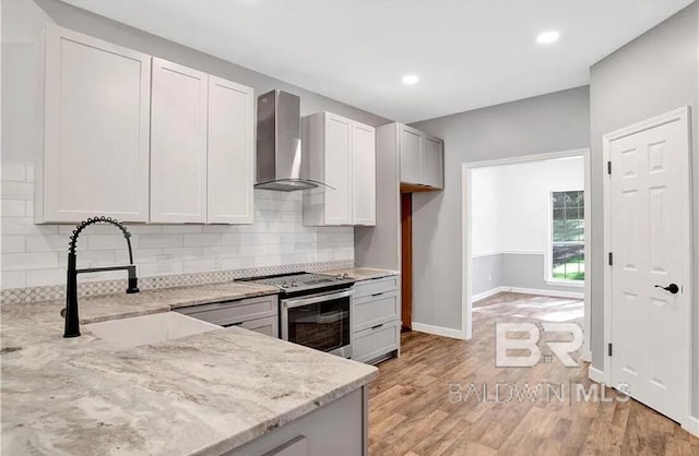 kitchen with sink, light stone counters, white cabinets, stainless steel electric stove, and wall chimney exhaust hood