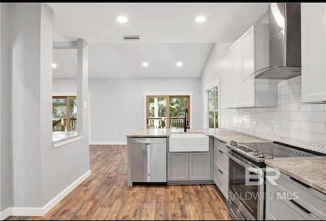 kitchen featuring wall chimney range hood, sink, appliances with stainless steel finishes, light hardwood / wood-style floors, and decorative backsplash