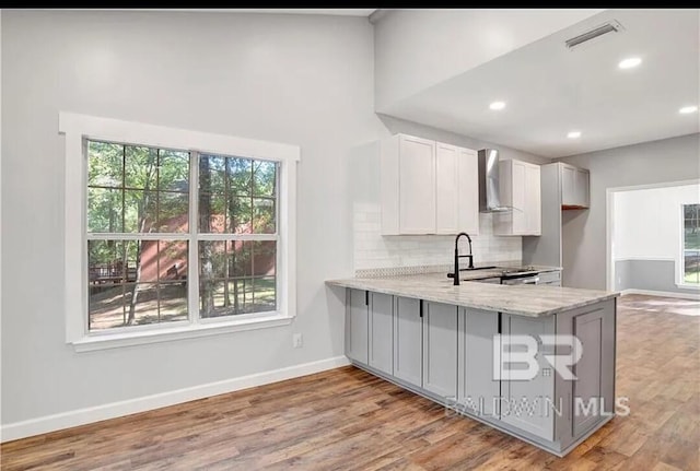 kitchen featuring wall chimney exhaust hood, kitchen peninsula, light stone countertops, and electric range