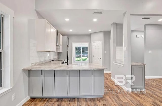 kitchen featuring gray cabinetry, light stone counters, light hardwood / wood-style flooring, kitchen peninsula, and backsplash