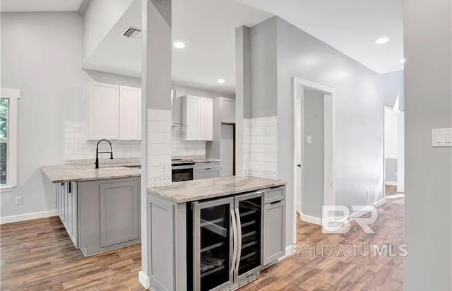 kitchen with light stone counters, tasteful backsplash, light hardwood / wood-style flooring, kitchen peninsula, and beverage cooler