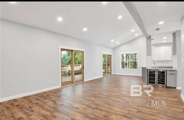 unfurnished living room featuring wine cooler, vaulted ceiling with beams, hardwood / wood-style floors, and sink