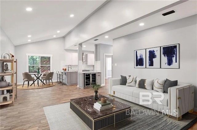 living room featuring lofted ceiling, sink, hardwood / wood-style floors, and beverage cooler