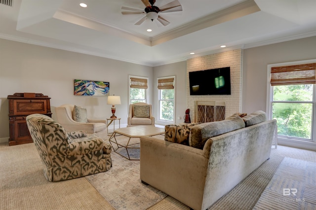 carpeted living room with ceiling fan, crown molding, a brick fireplace, and a tray ceiling