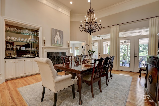 dining area featuring a chandelier, ornamental molding, french doors, light wood-type flooring, and a premium fireplace