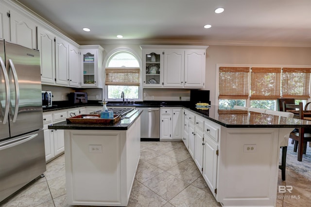 kitchen with dark stone counters, a kitchen island, white cabinetry, light tile patterned floors, and stainless steel appliances