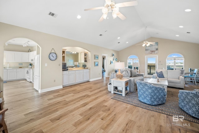 living area featuring visible vents, baseboards, light wood-type flooring, lofted ceiling, and arched walkways