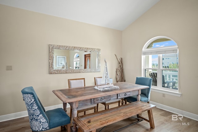 dining area featuring wood finished floors, baseboards, and vaulted ceiling