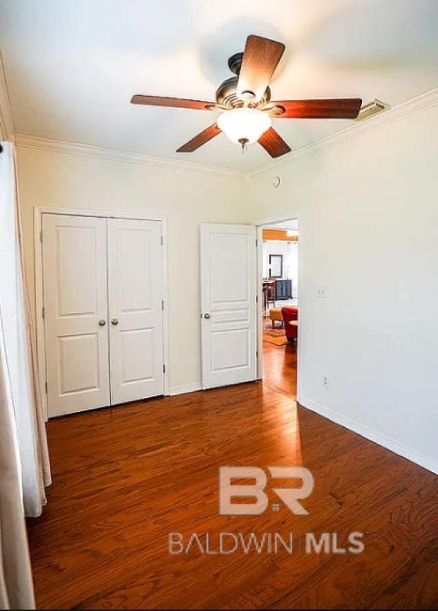 unfurnished bedroom featuring ornamental molding, dark hardwood / wood-style flooring, ceiling fan, and a closet